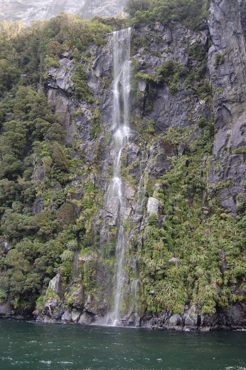 This is one of the many unnamed waterfalls in Milford Sound, New Zealand. They are likely 100 feet or 30 meters tall.
