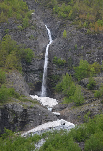 This is a taller waterfall in Nærøyfjord that plunges in multiple drops. There is snow at the base of the falls. 