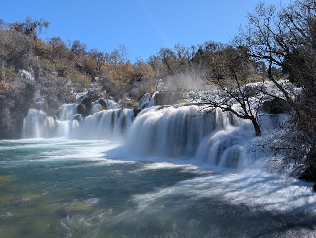 This is one view of Skradinski Falls, also known as Skradinski Buk, in March 2025. This shows a waterfall that is extremely wide and about 50-60 feet tall. 